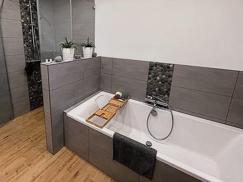 Badewanne mit umlaufender Verfliesung in Betonoptik und einem Streifen aus Kieselmosaik