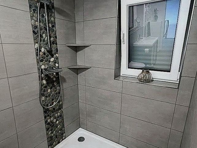 Dusche mit großformatigen Wandfliesen, senkrechtem Kieselmosaik-Streifen und Bodenbelag in Holzoptik
